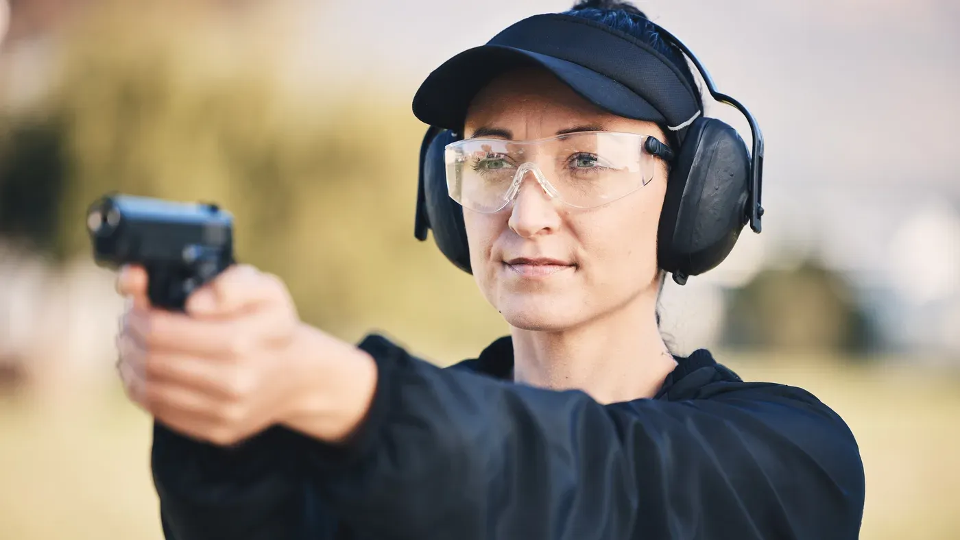 Skytt med skyddsglasögon och hörselkåpor siktar pistol
