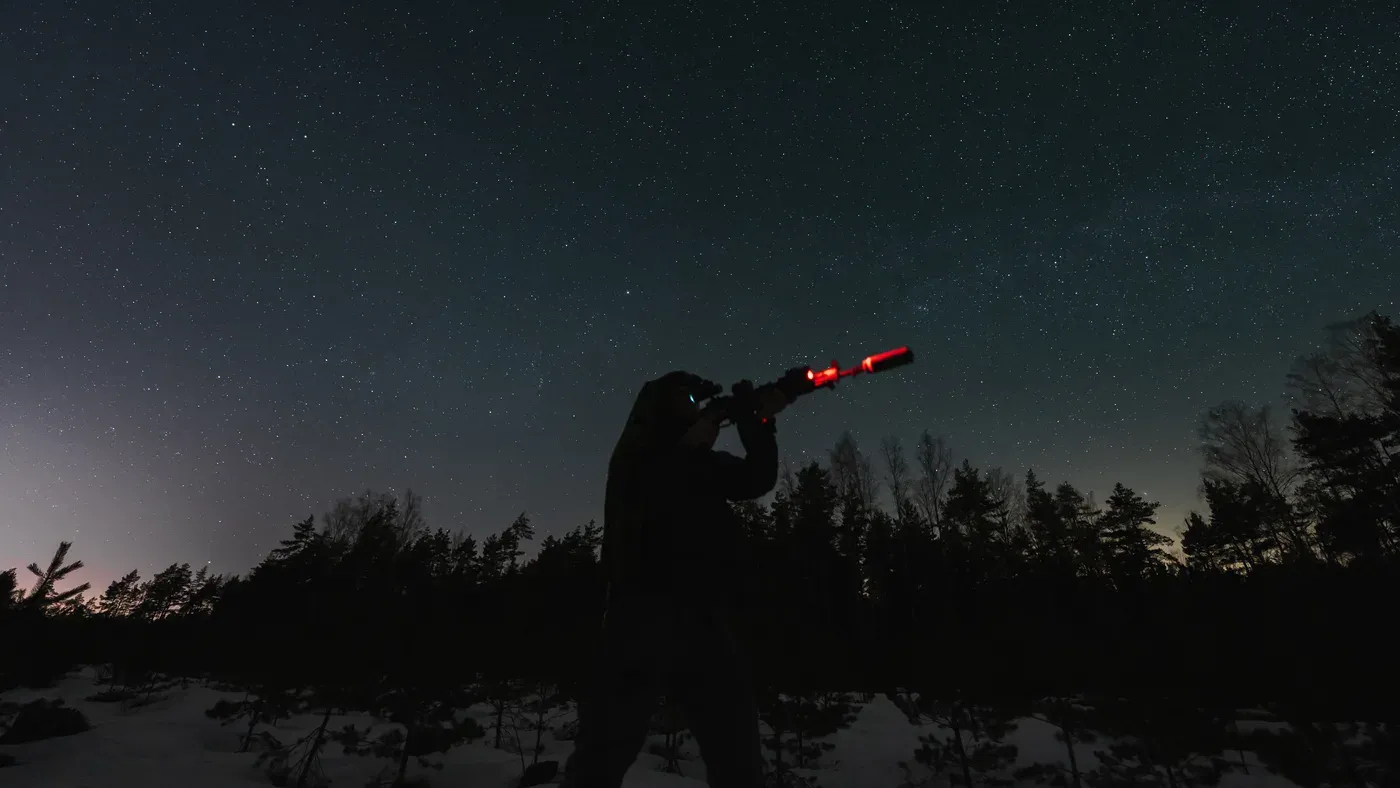 Jägare siktar med rödpunktbelyst gevär mot stjärnhimmel