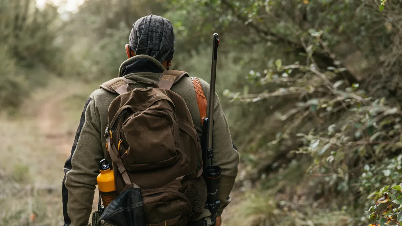 Jägare med jaktryggsäck och vapen på ryggen i skogsterräng